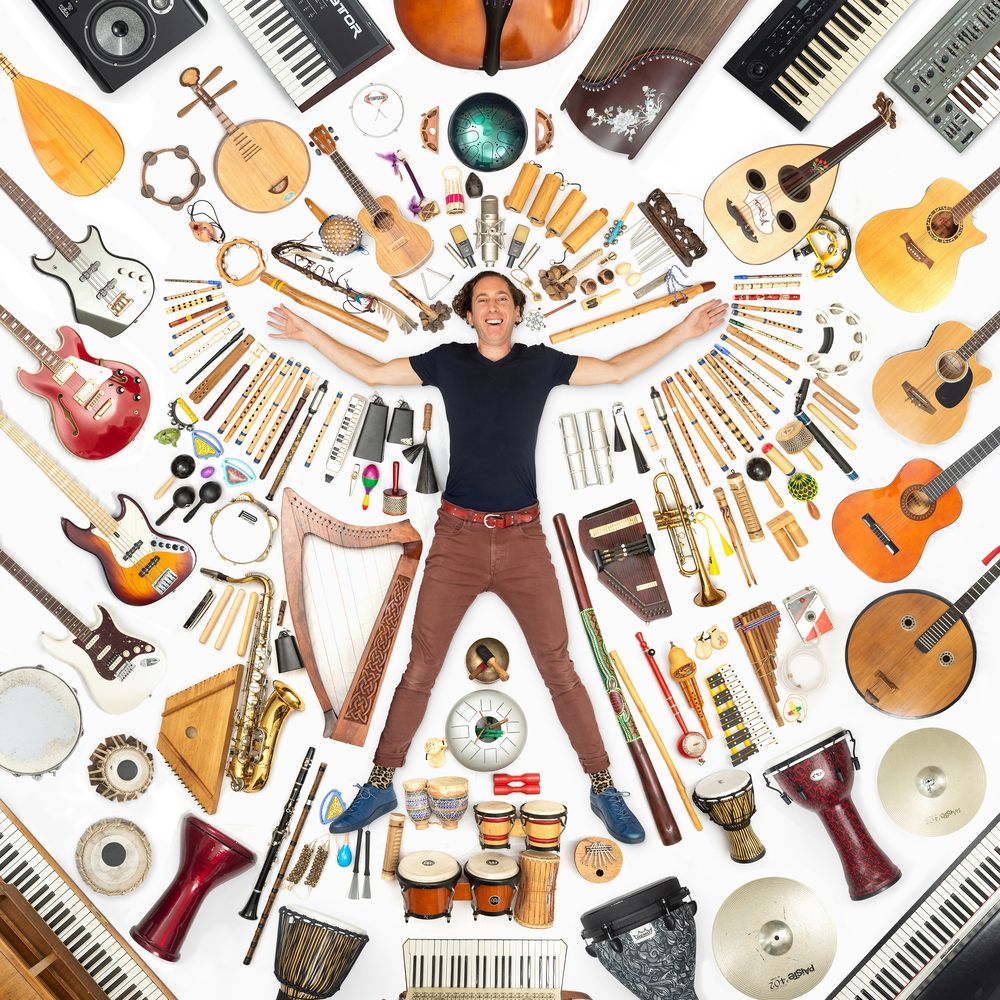 Marc JB lying on the floor surrounded by his guitars, keyboards, harps, flutes and drums